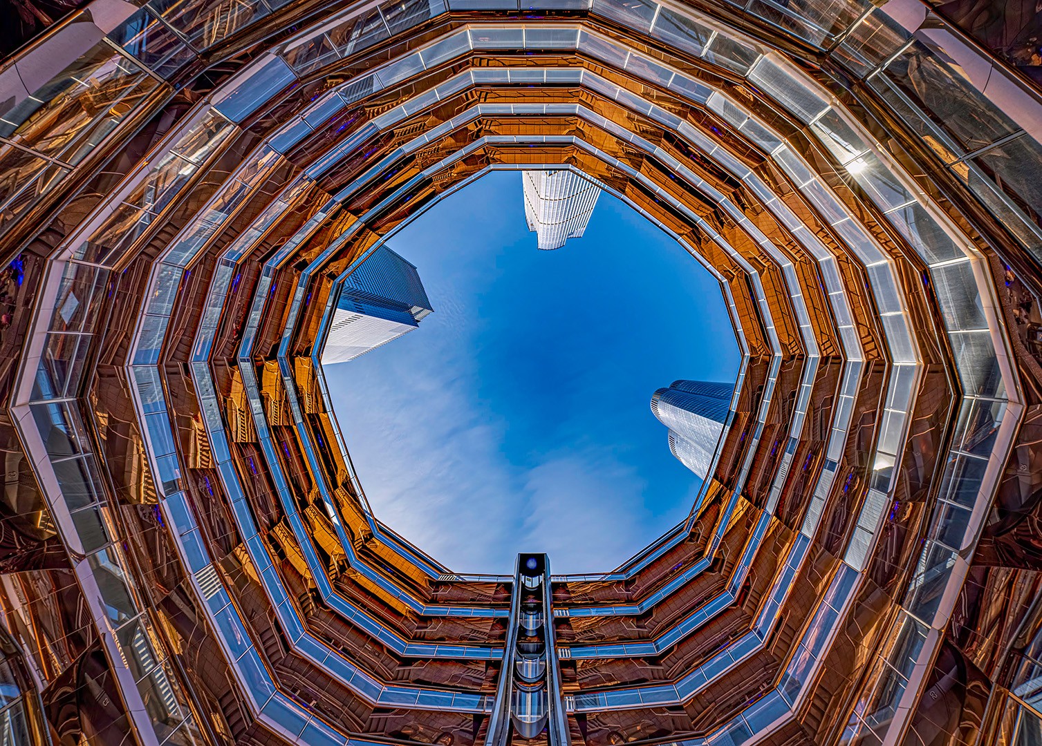 Looking up through a circular building's open center, multiple floors with glass and metal railings surround the sky.
