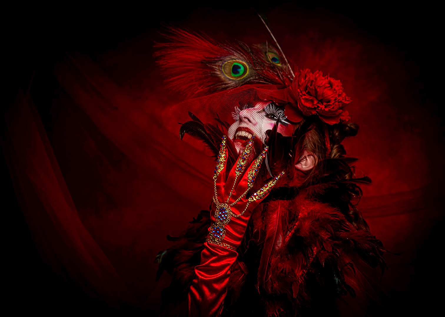 Person with elaborate red costume, feathered mask, and red flower, holding a hand to face with jewelry, against a dark red background.
