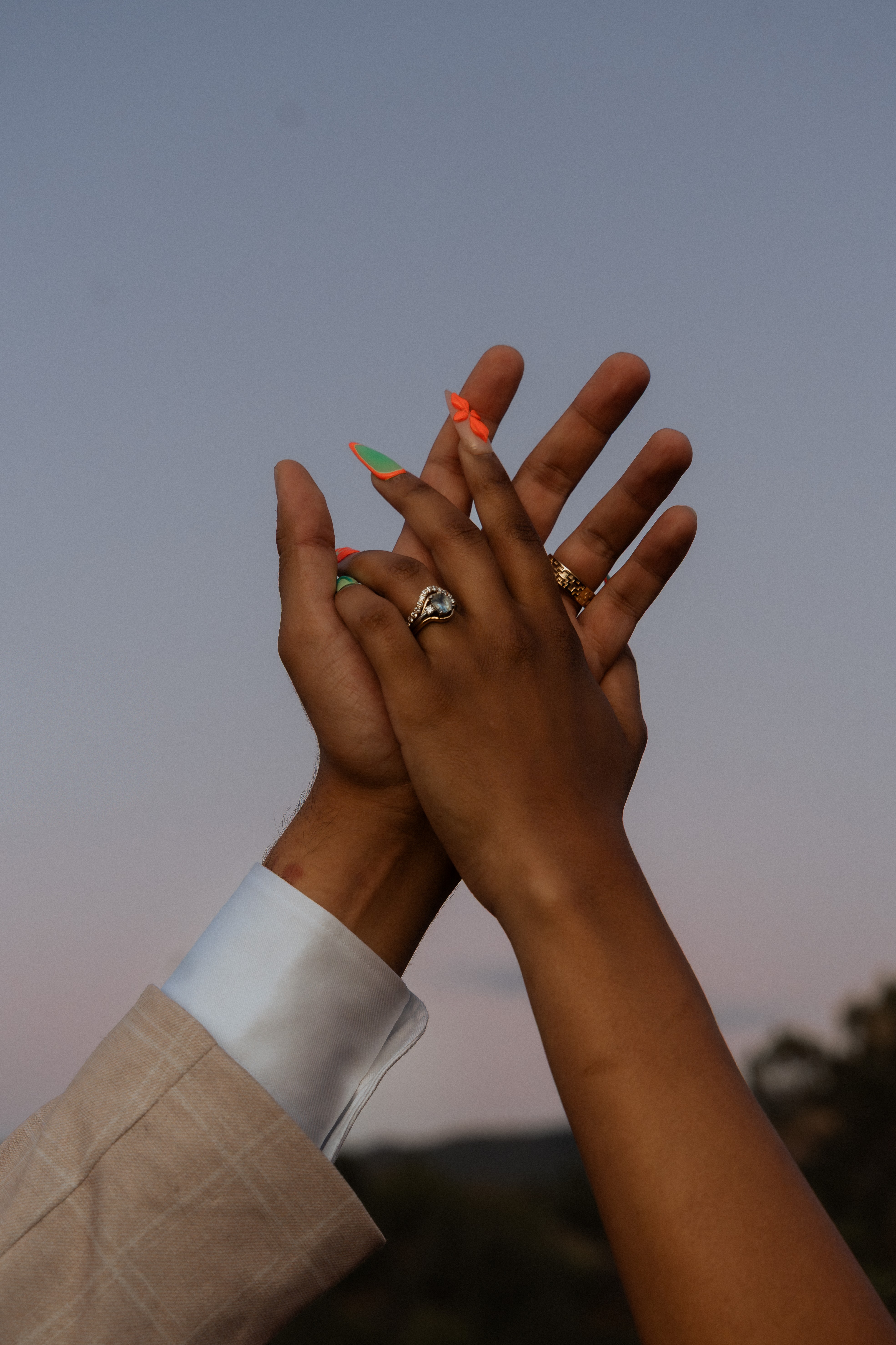 Two hands with rings and painted nails touch against a clear sky background.