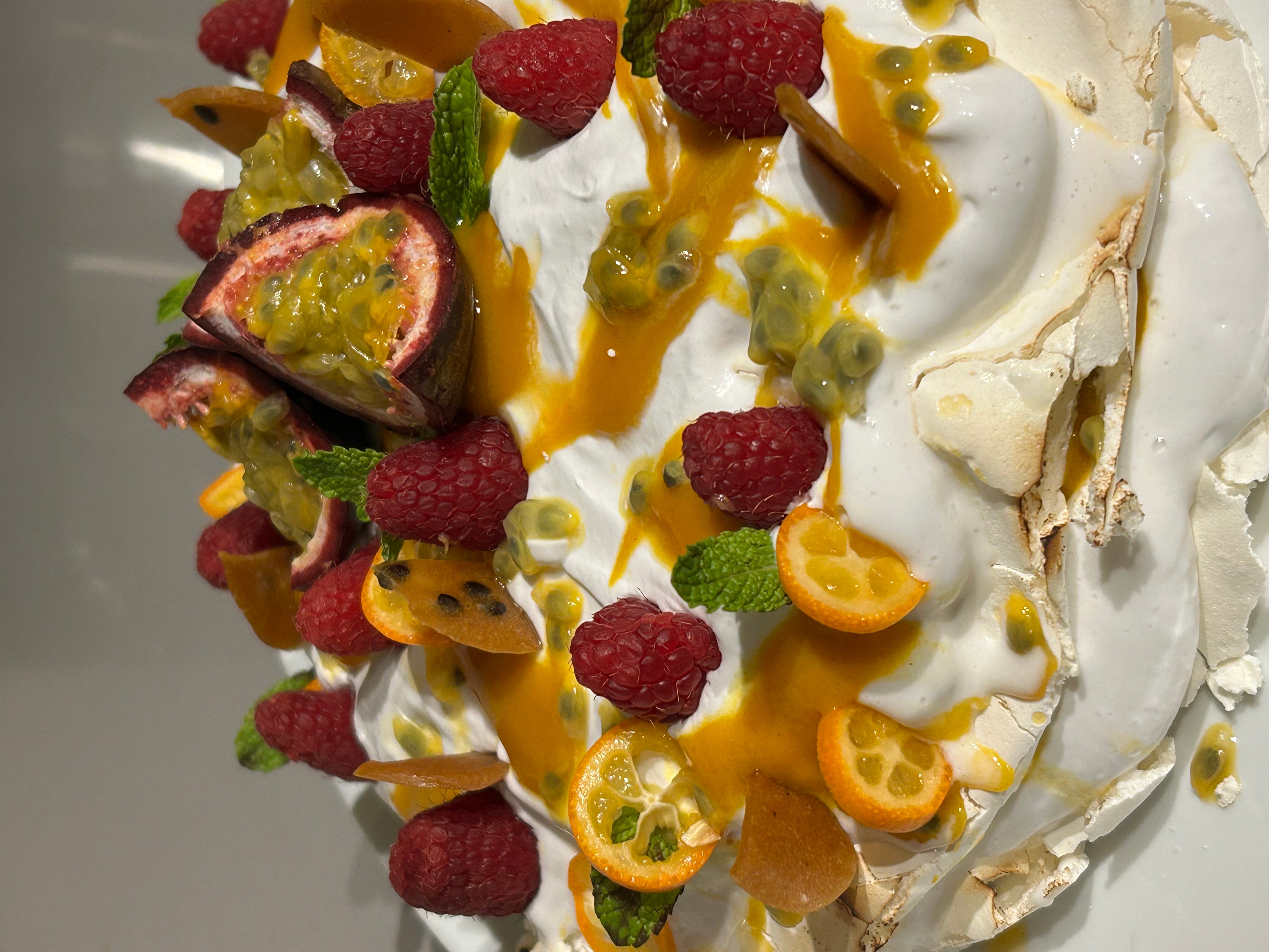A cake decorated with various fruits including raspberries, passion fruit, kumquat, and mint leaves, topped with white frosting and drizzled with caramel.