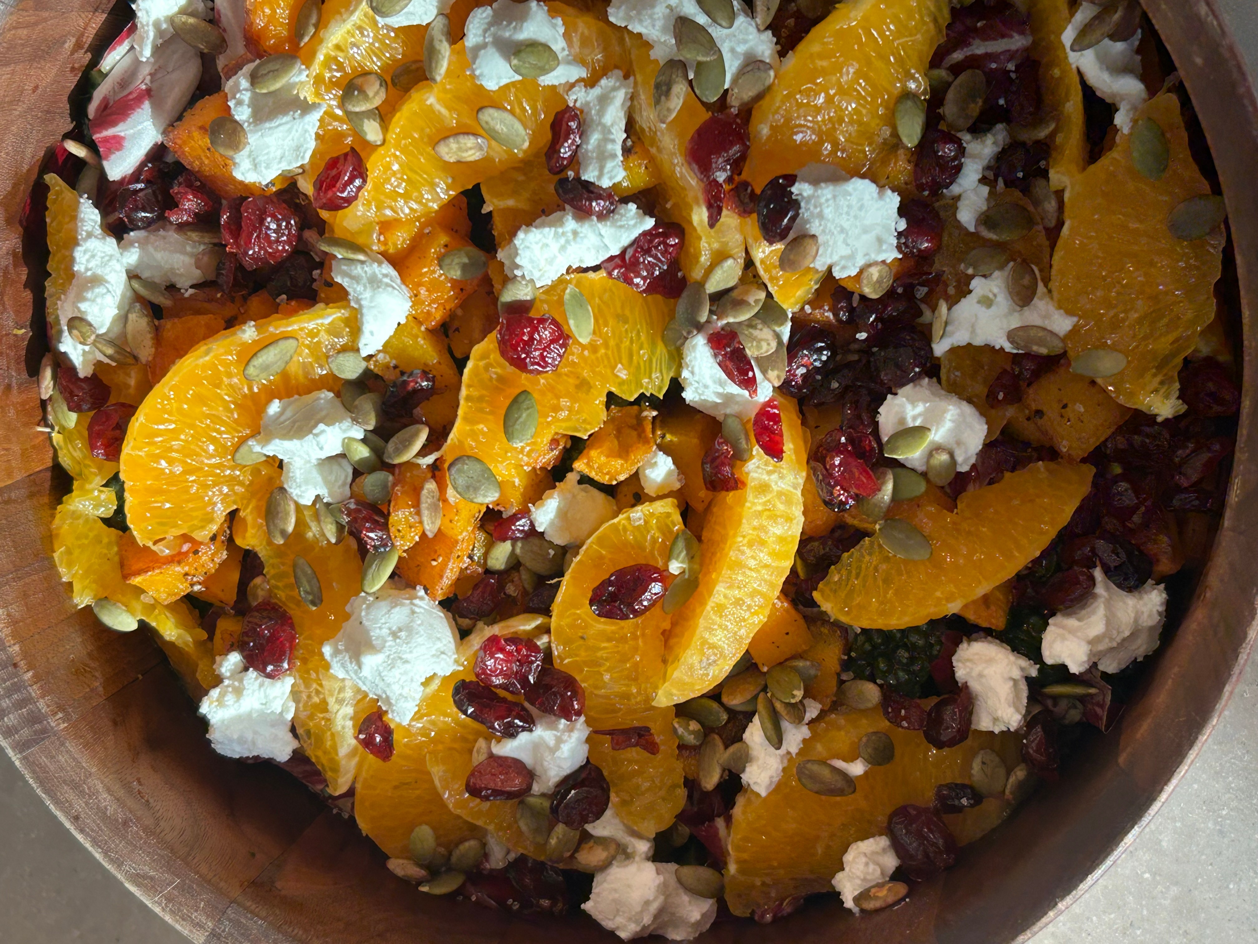 Fruit salad with orange slices, dried cranberries, and white cheese chunks in a bowl.
