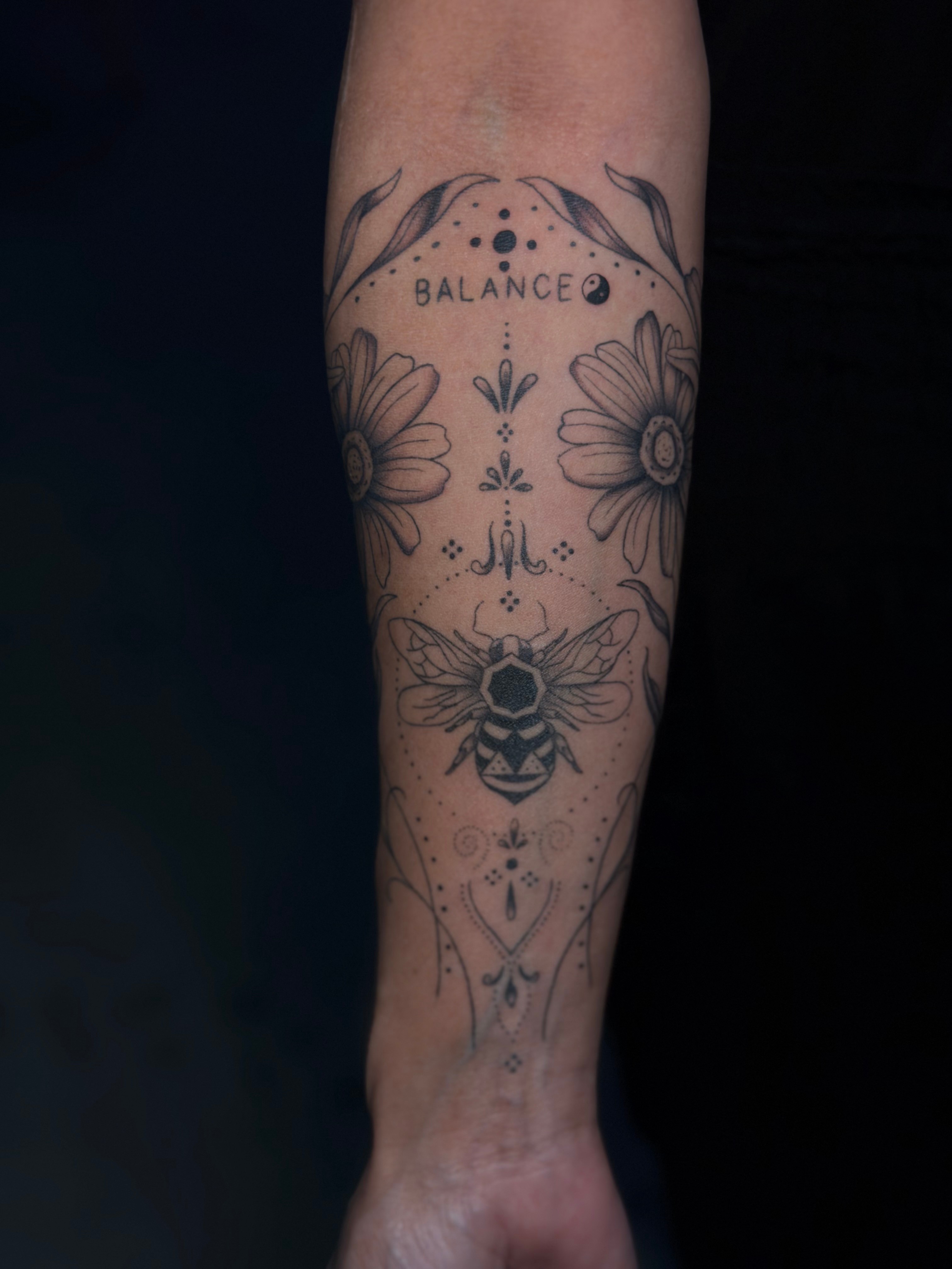 Tattoo of a bee, flowers, and the word 'BALANCE' on a person's forearm.