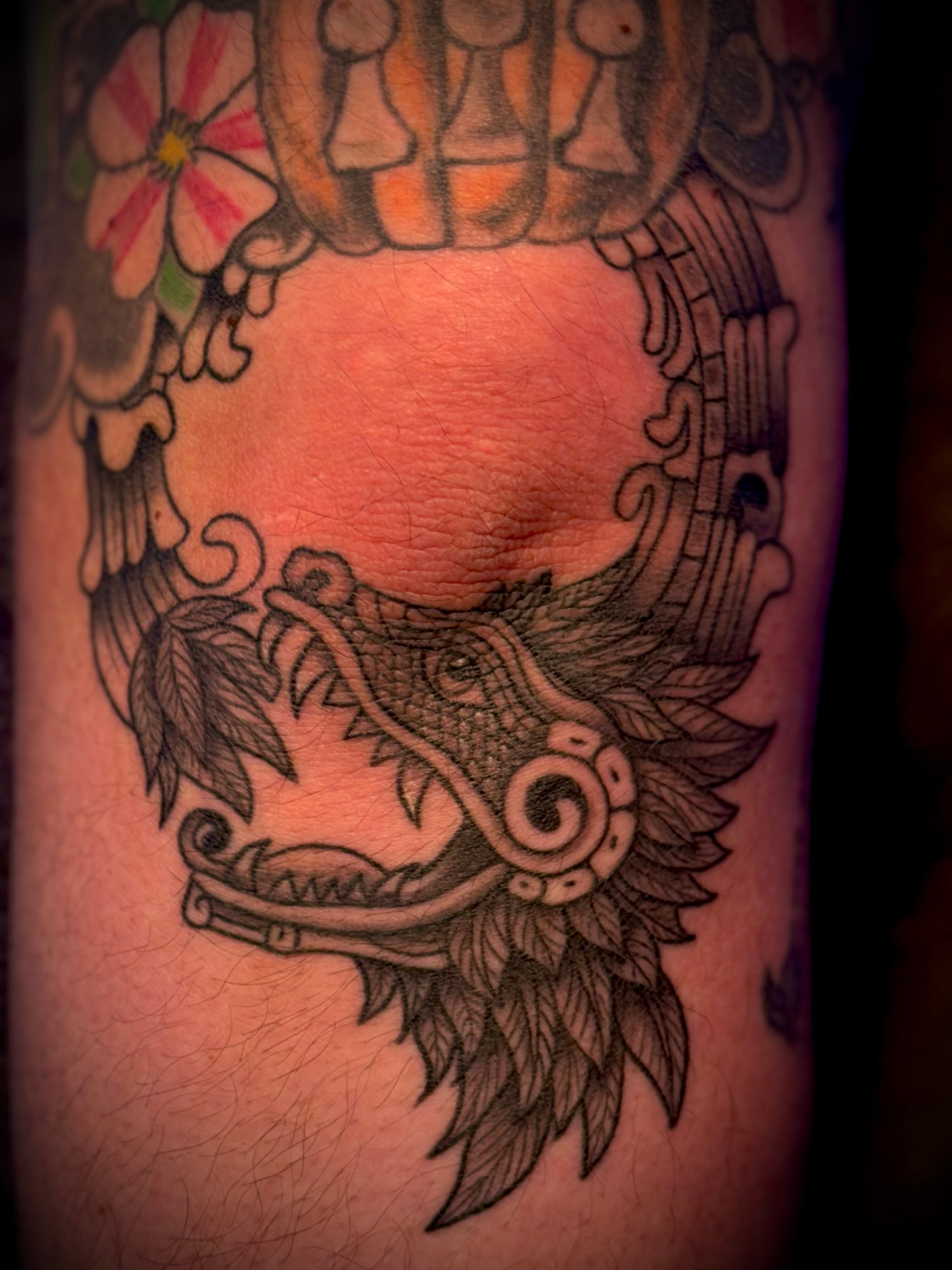 Tattoo of a dragon's head with detailed scales and mane on skin, with colorful floral designs above.