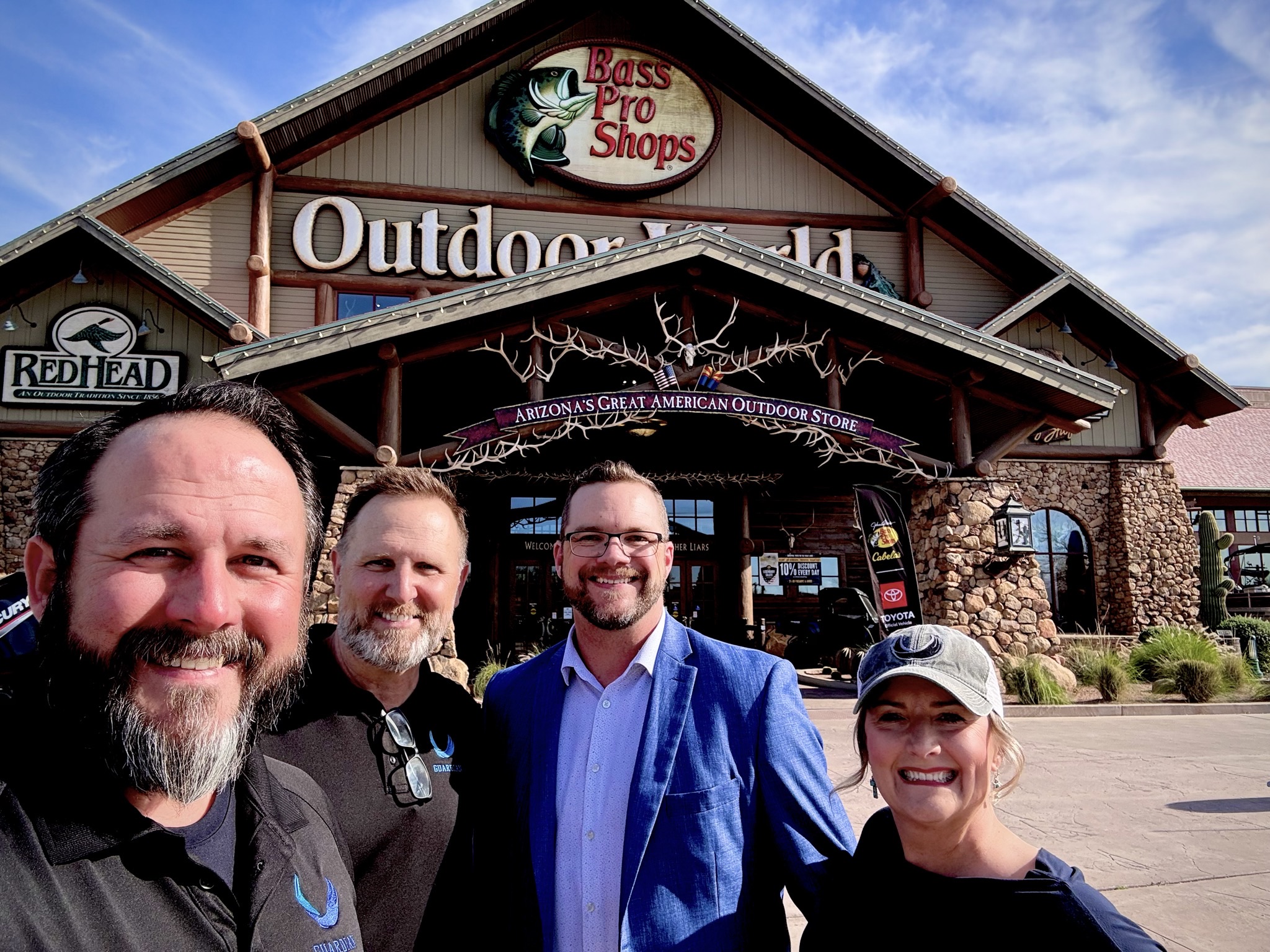 Four people standing in front of a store with a sign reading 'Bass Pro Shops' and 'Outdoor World'.