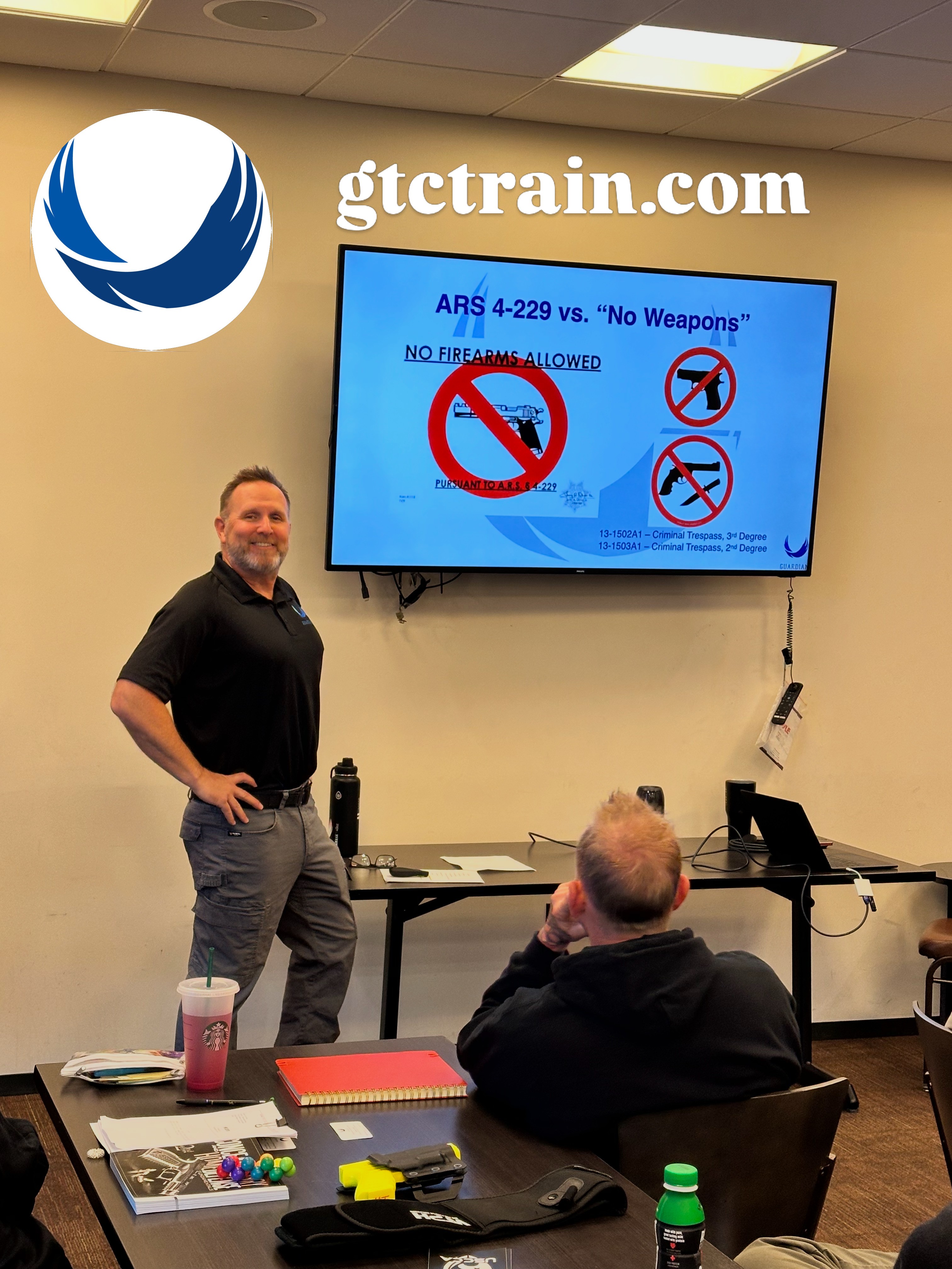 Man standing in front of a presentation screen with a seated audience in a classroom setting.