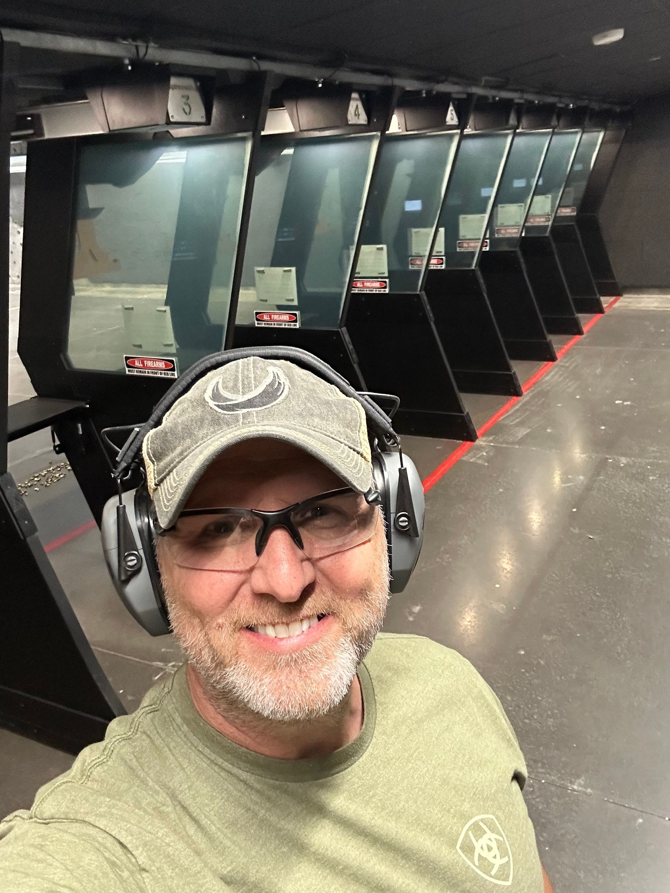 A man wearing a cap, glasses, and headphones takes a selfie in front of multiple ATM machines inside a bank or ATM area.