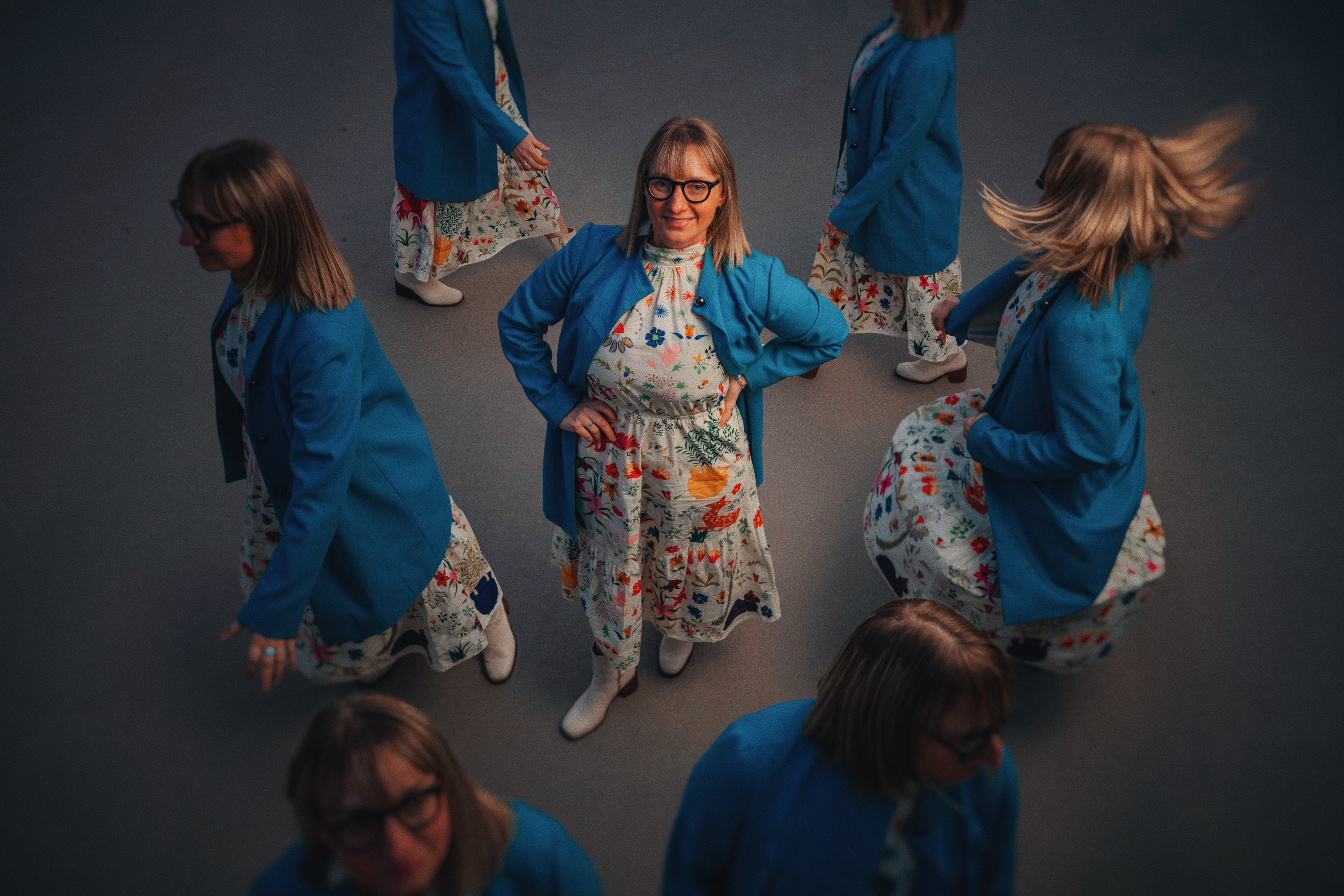 Group of children wearing blue jackets and floral dresses, standing and walking on a dark background.
