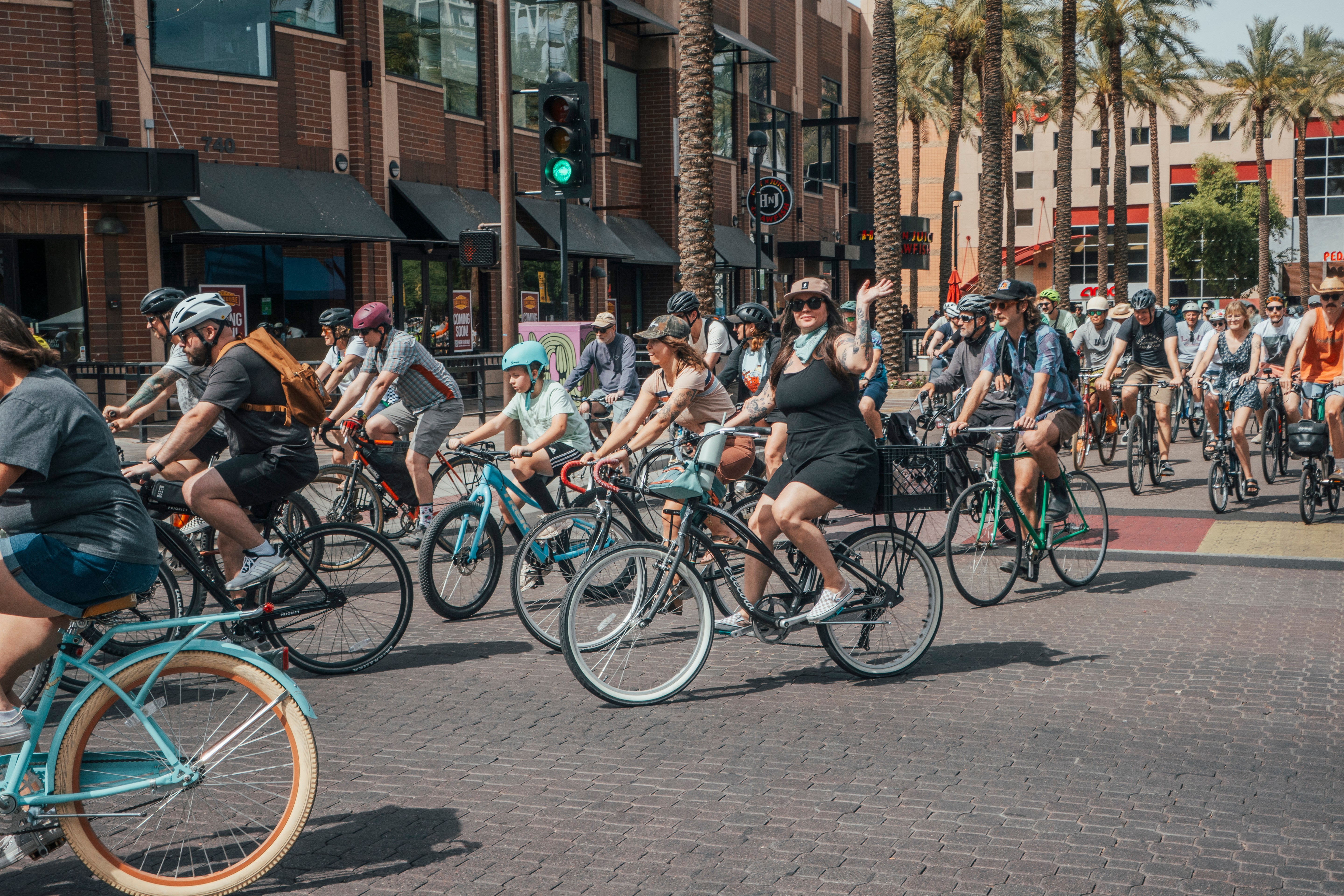 Group of people riding bicycles on a city street with buildings and palm trees in the background.
