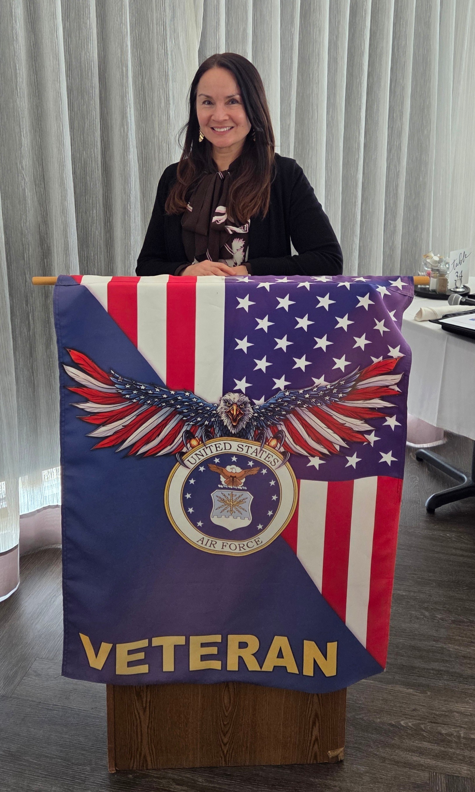 Woman standing behind a veteran-themed banner with an eagle, American flag, and the word VETERAN.