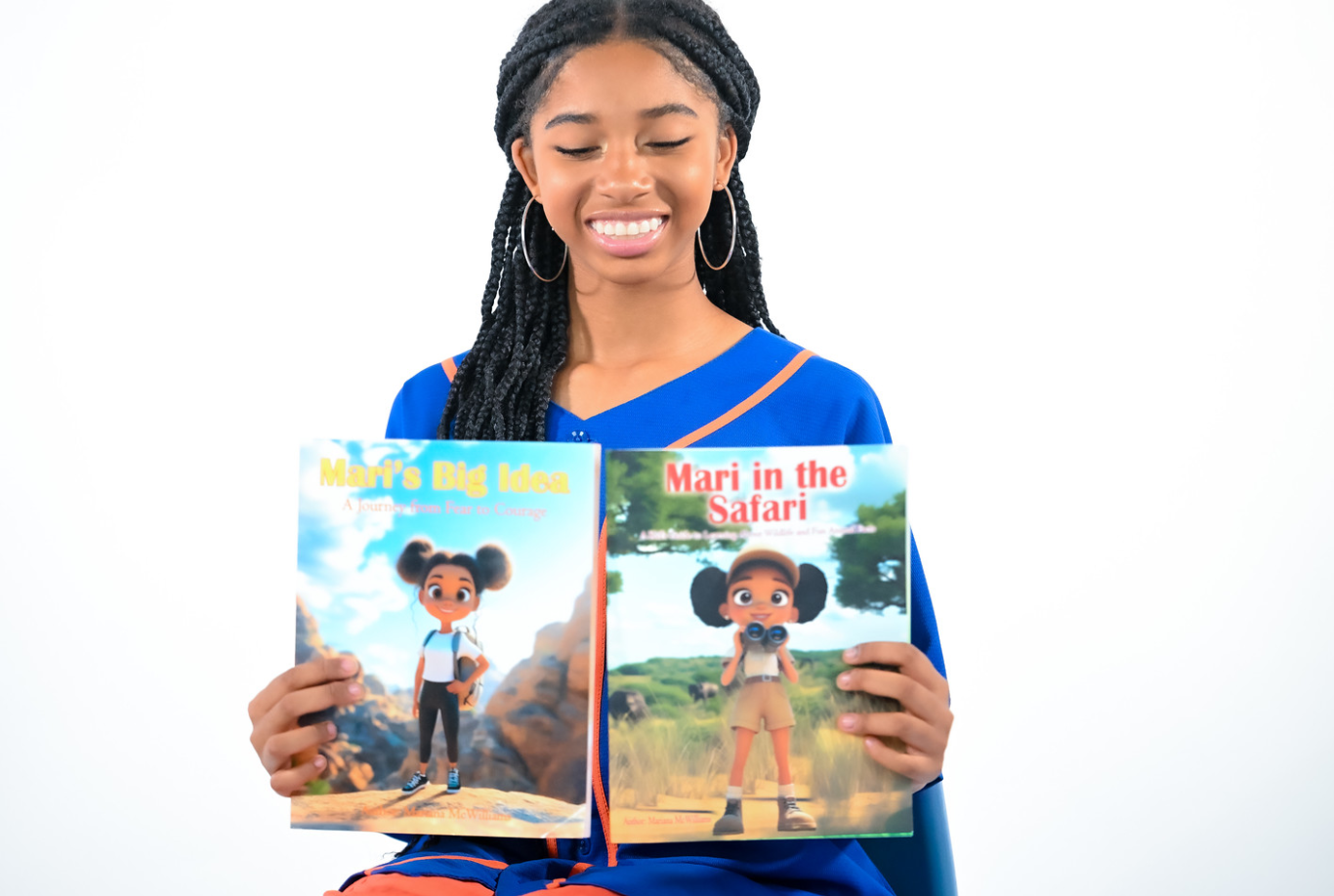 Young girl with braided hair smiling, holding two children's books, one titled 'My Big Moon' and the other 'Mari in the Safari'.