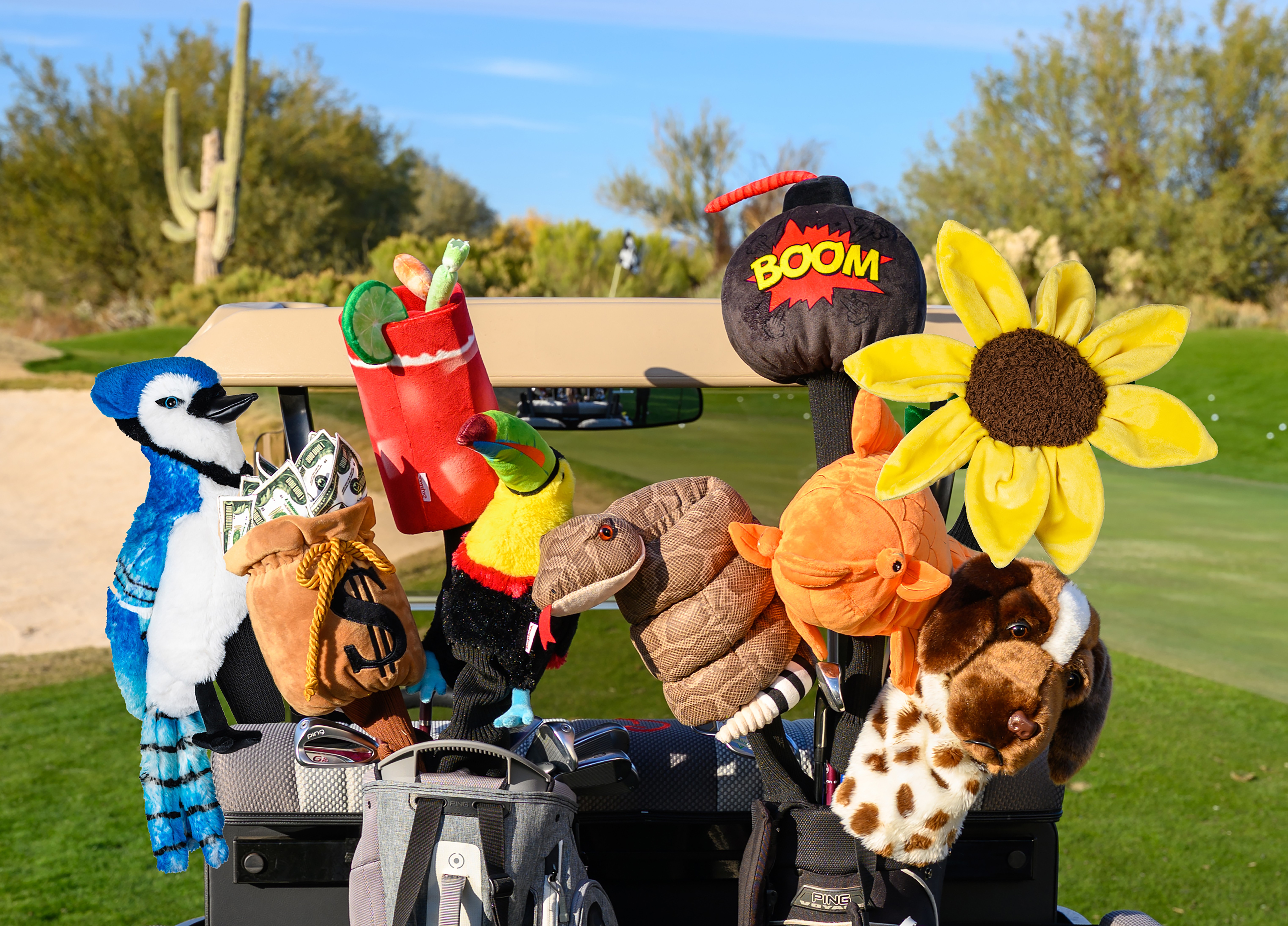 Group of colorful plush puppets in a golf cart outdoors with trees and a cactus, some holding objects like a sunflower and a balloon.