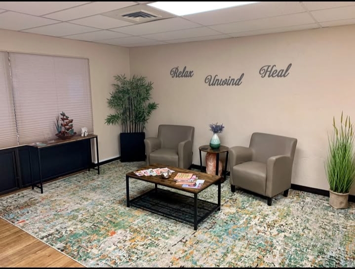 Waiting area with two armchairs, a coffee table, plants, and wall decor reading 'Relax Unwind Heal'.