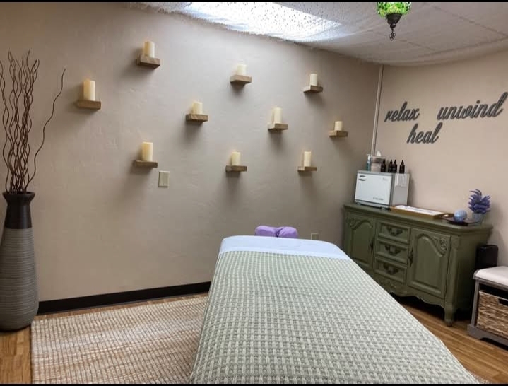 Massage table in a room with wall candles, a green cabinet, and wall words 'relax unwind heal'.
