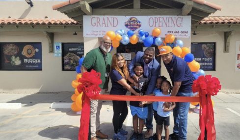 Group of people at grand opening with balloons and ribbon outside a building, smiling and holding scissors, children in front.