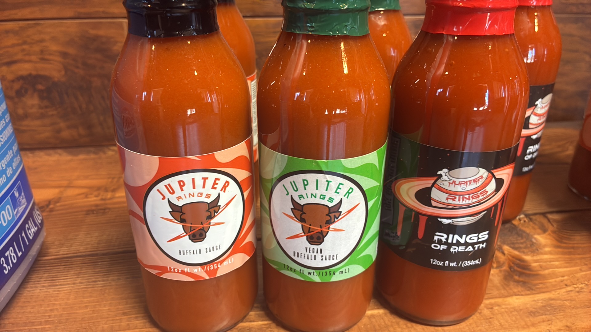 Three bottles of hot sauce with different labels and colors on a wooden surface.