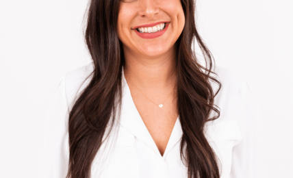 Young woman with long dark hair smiling, wearing a white blazer against a plain white background.