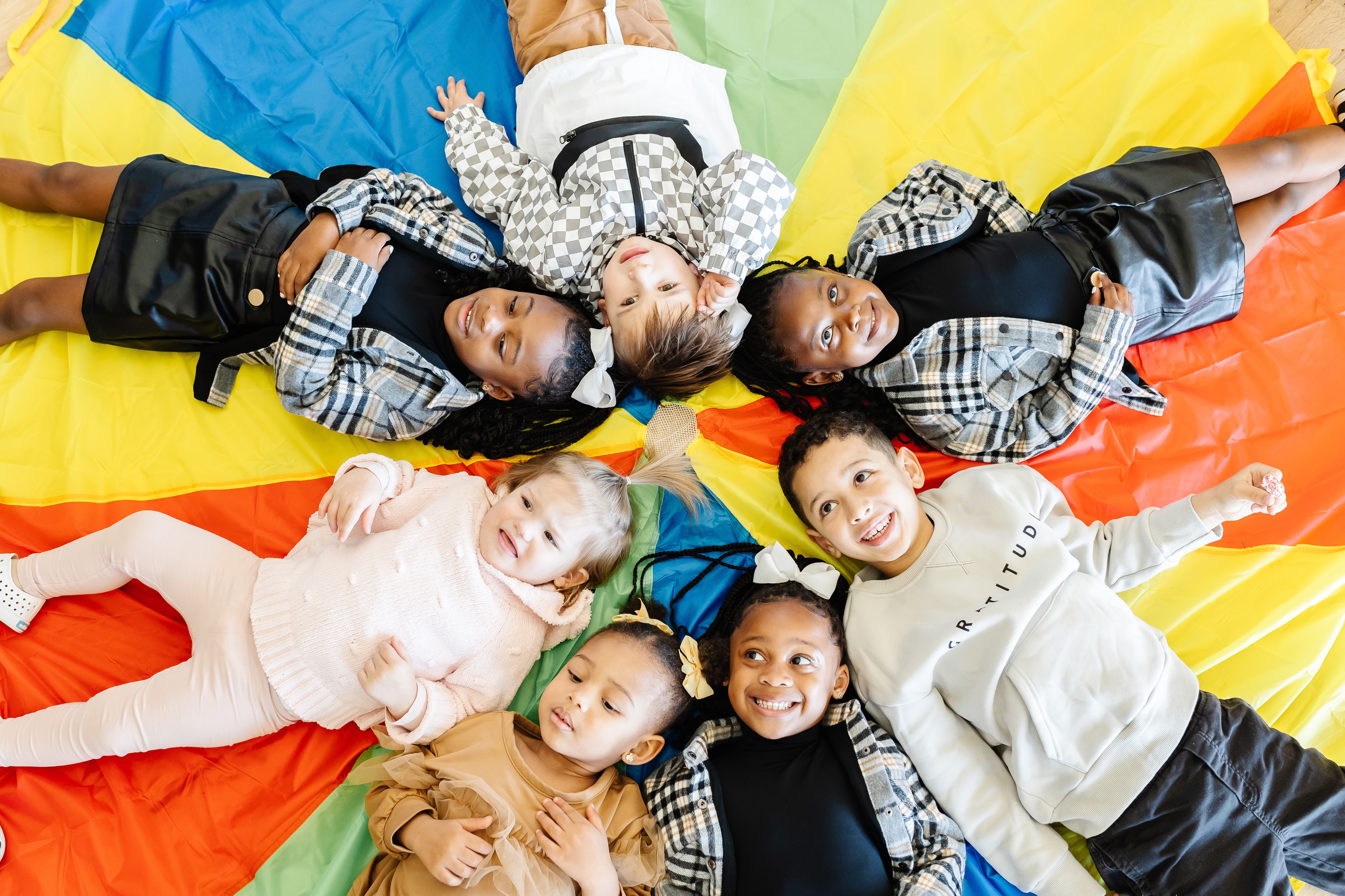 Group of children lying on colorful fabric, smiling and looking up at the camera.