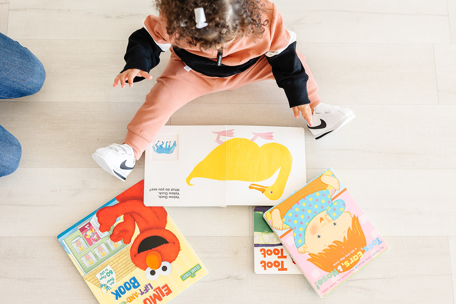 Child sitting on floor with books and a colorful drawing, viewed from above.