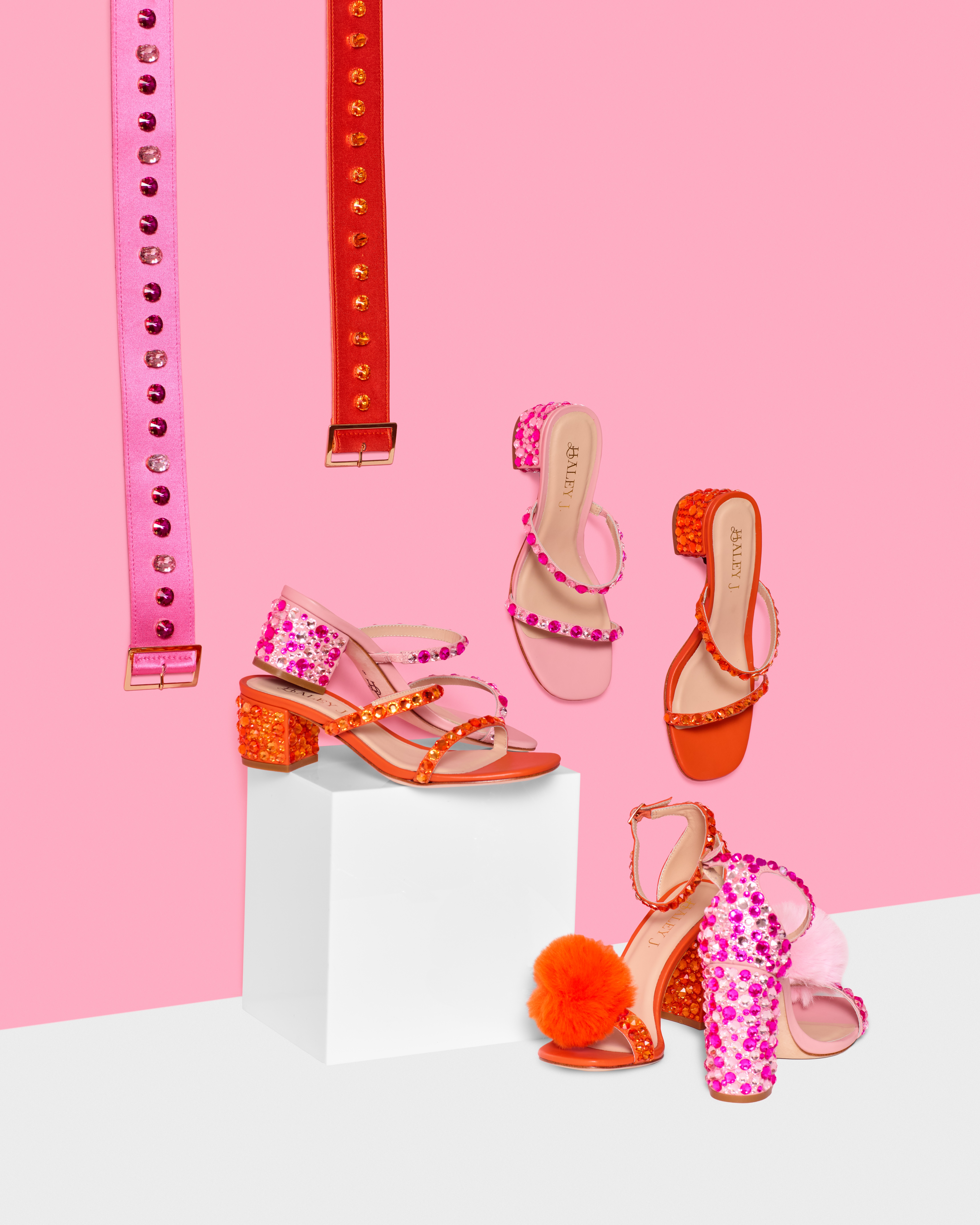 Display of colorful sandals and high heels against pink background, with some shoes on a white pedestal.