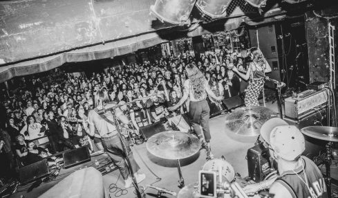 Band performs on stage with audience watching, musical instruments visible, in black and white, lively concert scene.