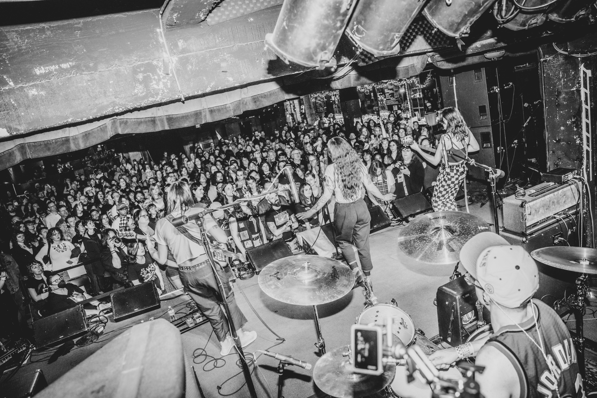 Band performs on stage with audience watching, musical instruments visible, in black and white, lively concert scene.