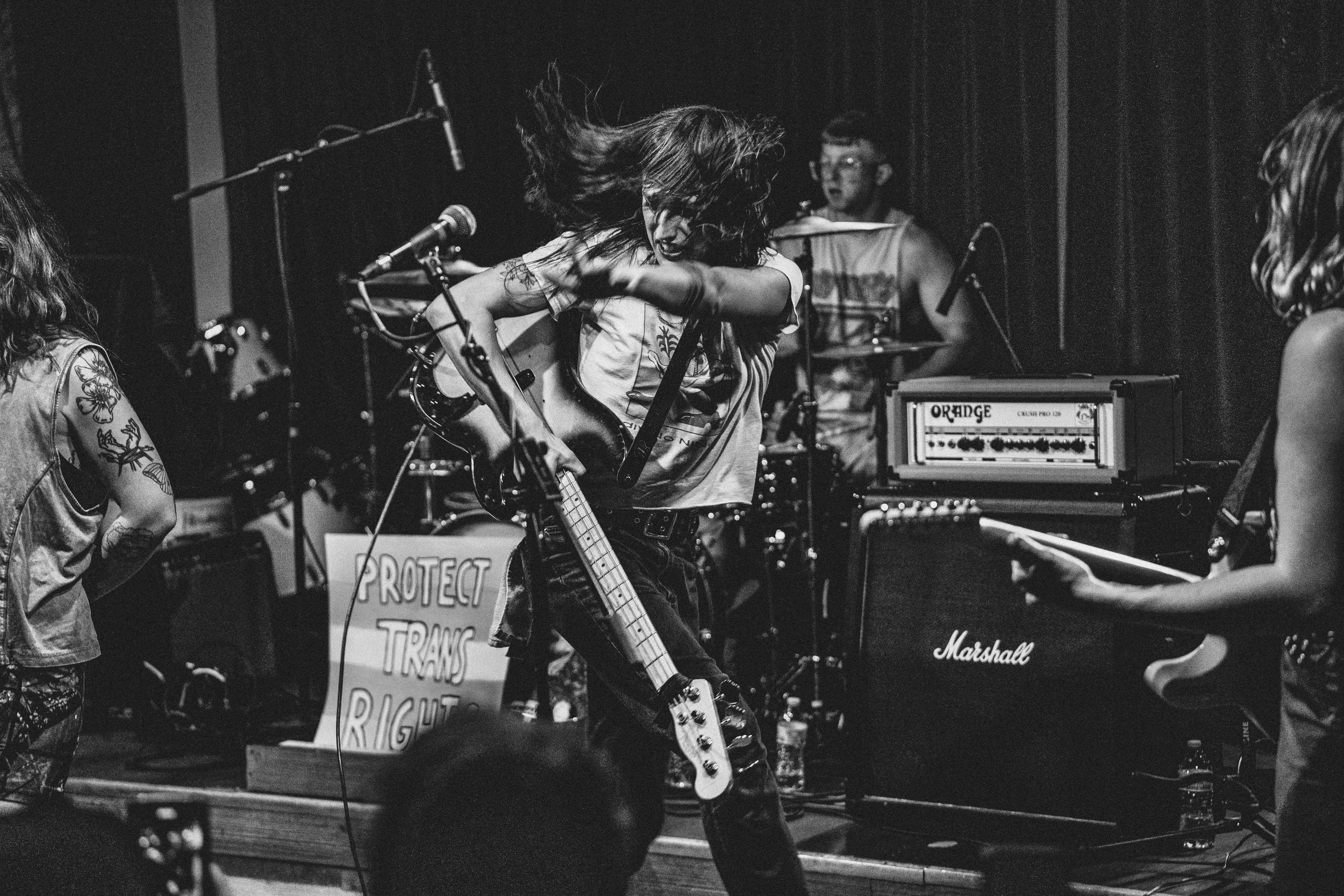 Band performing on stage with musical instruments and equipment, including guitars and amplifiers, in black and white.