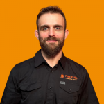 Portrait of a man with a beard and short hair, wearing a black shirt with a logo, against an orange background.