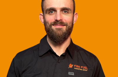 Portrait of a man with a beard and short hair, wearing a black shirt with a logo, against an orange background.