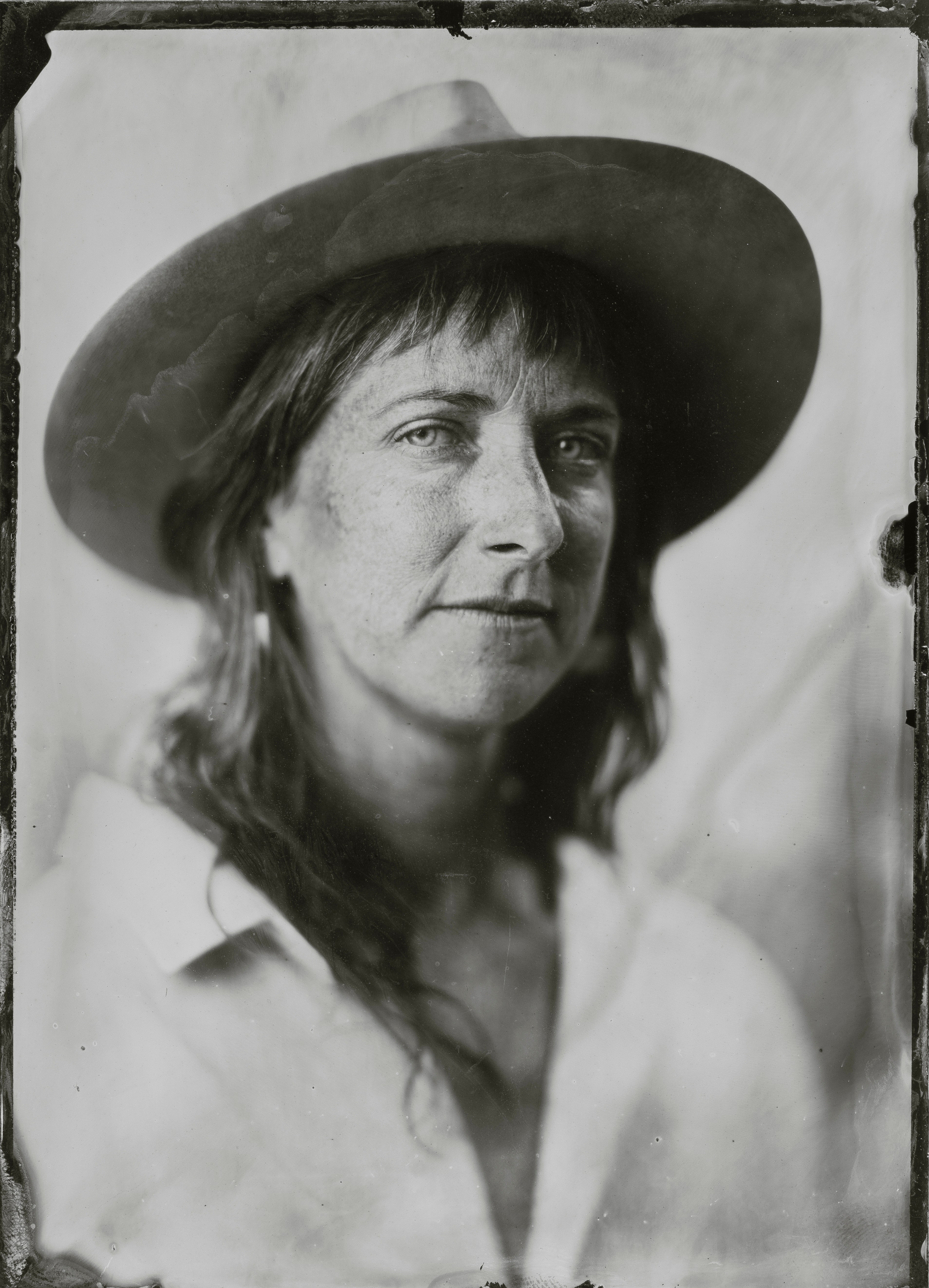 Woman with long hair wearing a wide-brimmed hat, looking at the camera, in black and white.