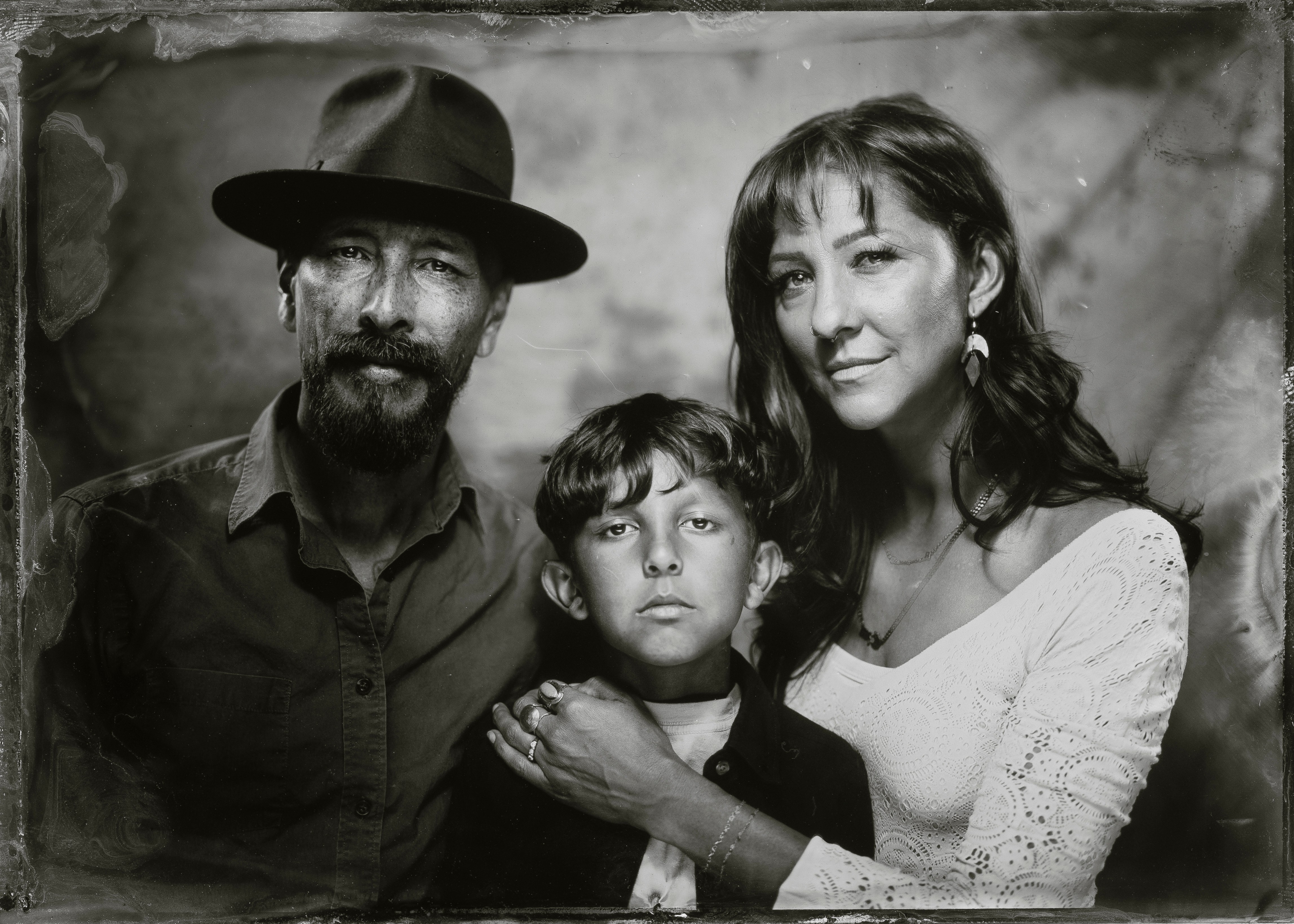 Three people, a man, a woman, and a child, pose together in a black-and-white photo, with the woman and child smiling.