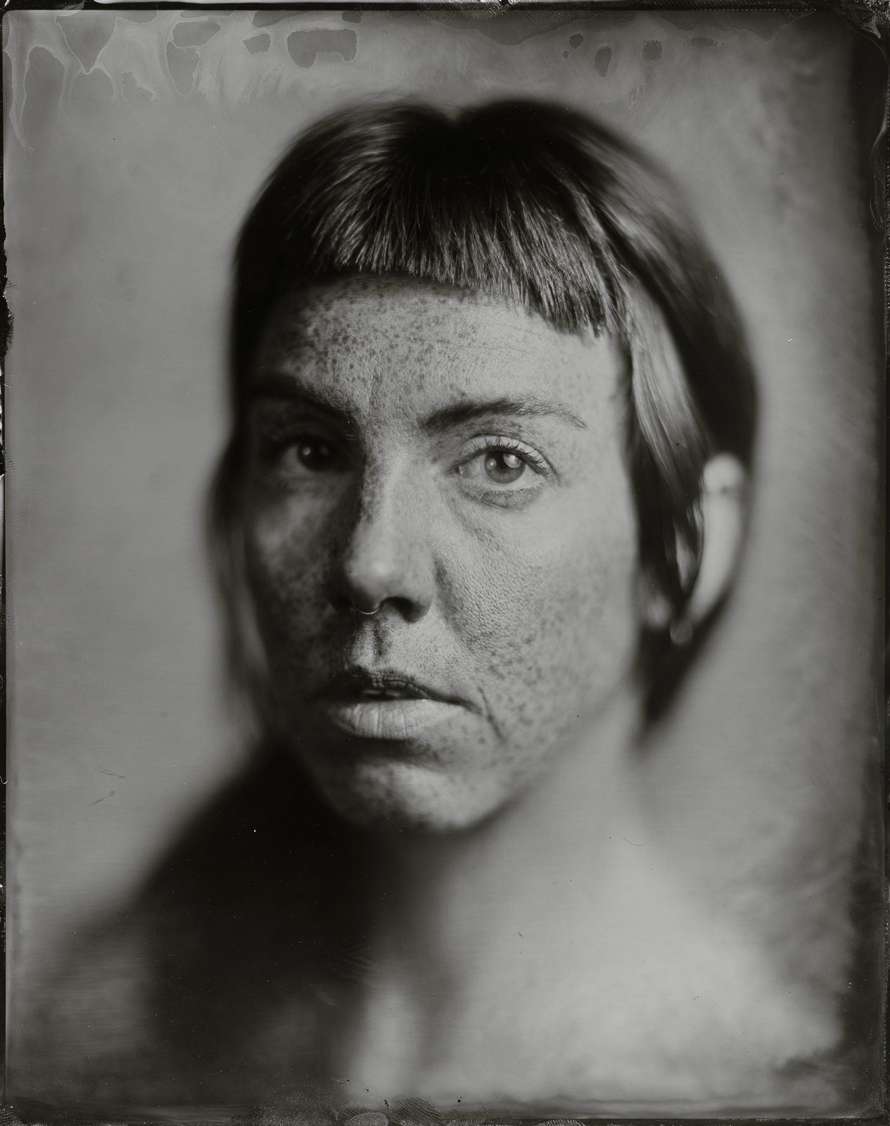 Black and white portrait of a person with short hair and freckles, facing forward with a neutral expression.